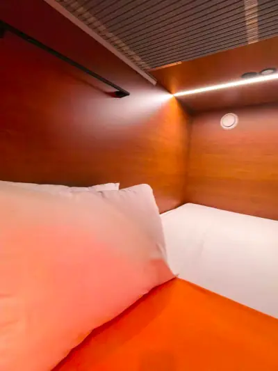 Cama inferior pod doble GettSleep almohada blanca ropa naranja techo madera Terminal C